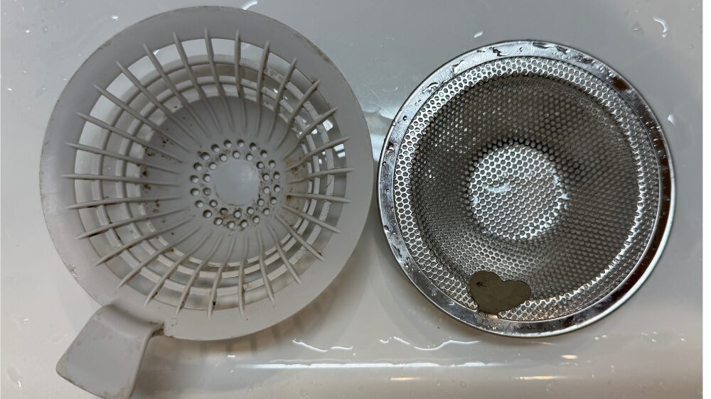 使用済みのプラスチック製排水口カバーと新しいステンレス製排水口カバーを取り外して並べて比較した写真